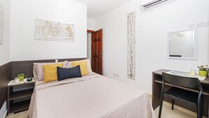 A modern bedroom with a bed, bedside tables, a desk, and an air conditioning unit. - Summer Breeze Superior Apartment with Terrace by Getaways Malta (Mellieha)