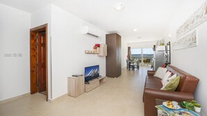 A modern living room with a brown leather sofa, a TV, and a dining area in the background. - Summer Breeze Superior Apartment with Terrace by Getaways Malta (Mellieha)