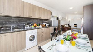 A modern kitchen with wooden cabinets, a built-in washing machine, and a dining area with a table set for four. - Summer Breeze Superior Apartment with Terrace by Getaways Malta (Mellieha)