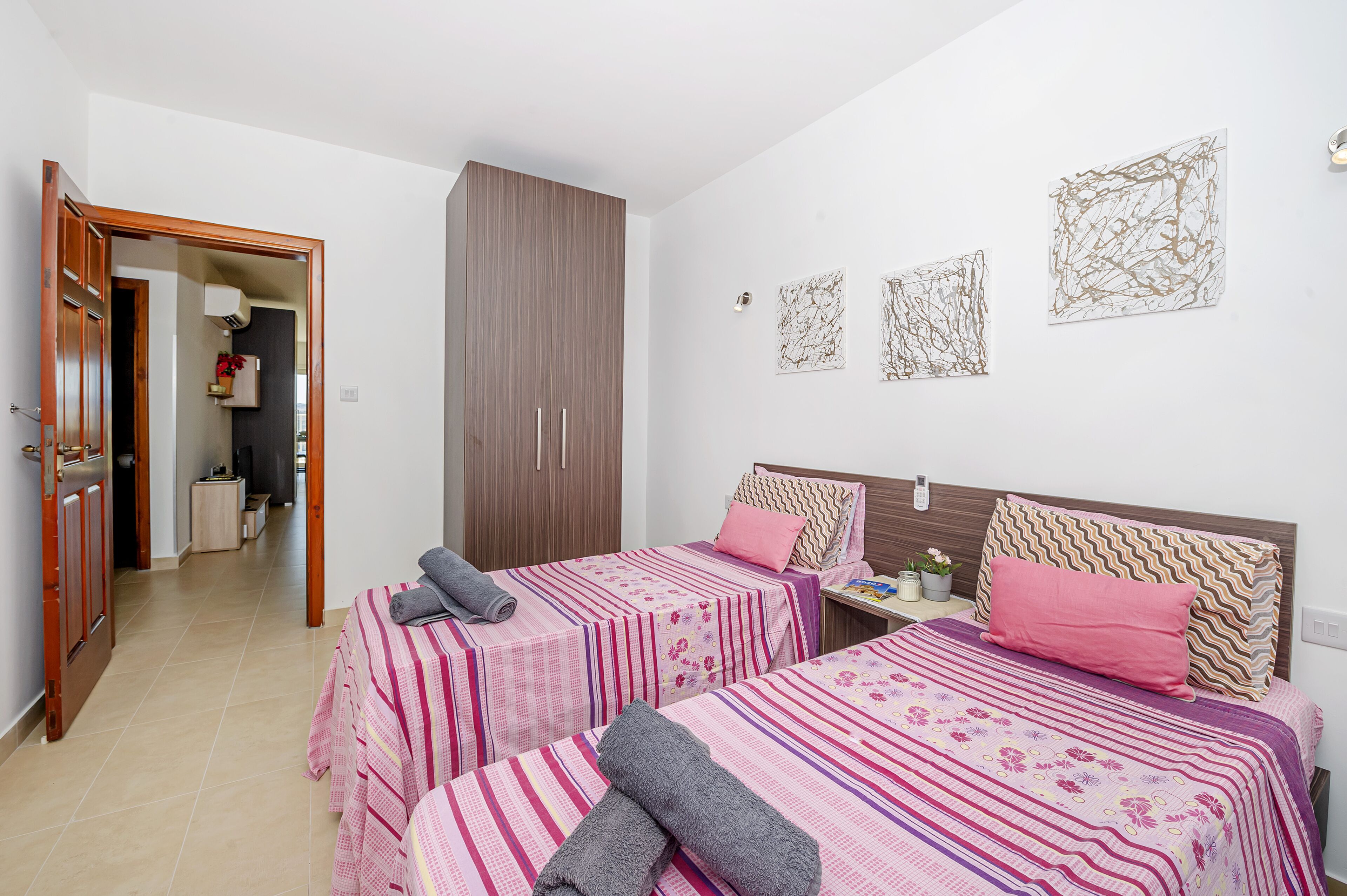 A bedroom with two beds, a wardrobe, and artwork on the wall.