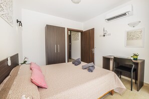 A hotel room with a bed, a desk, and an air conditioning unit.