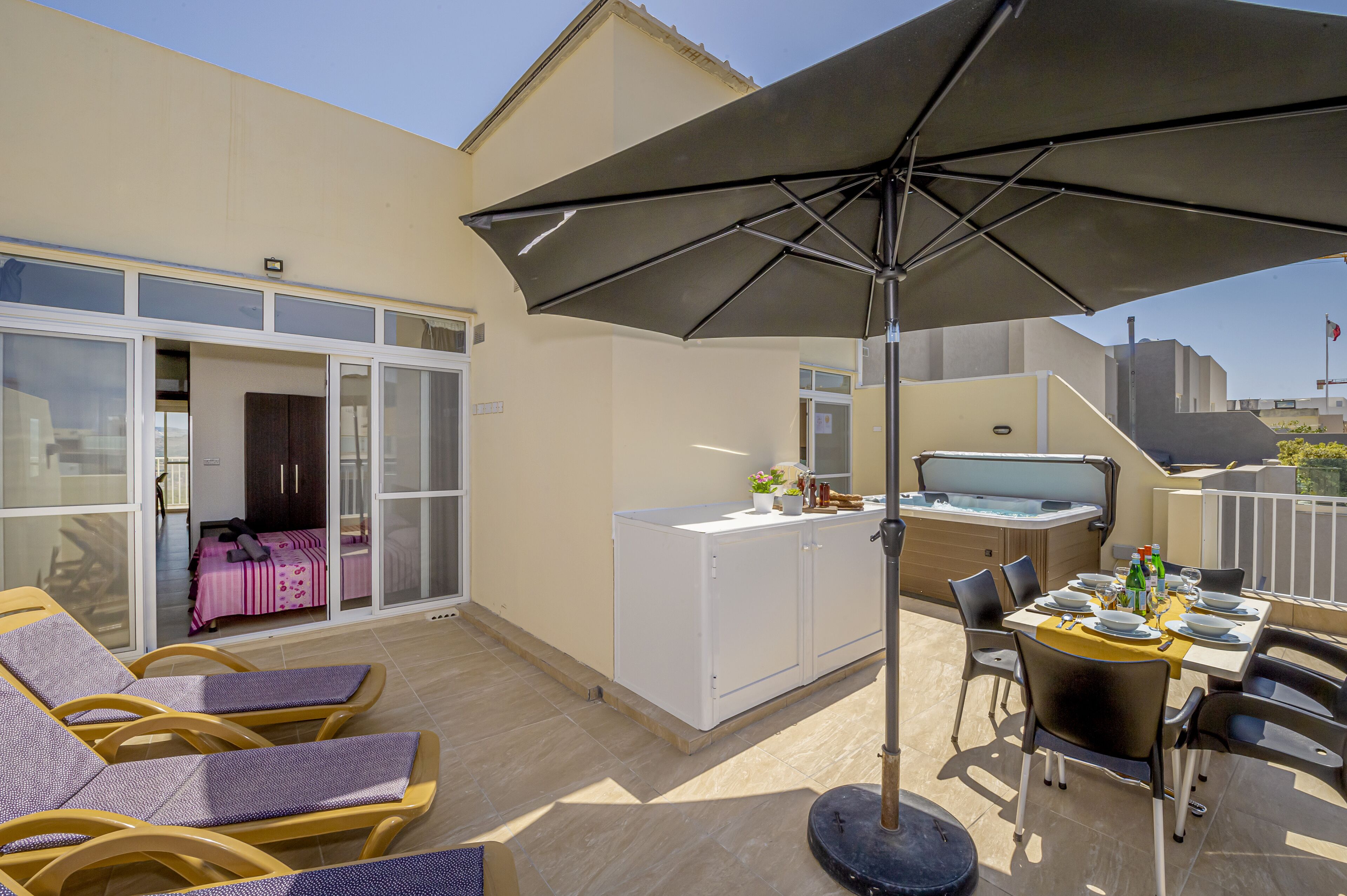 A balcony with a table set for dining, a sofa, and a large umbrella.