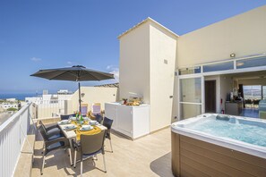 A balcony with a dining table, chairs, and an umbrella, overlooking a cityscape and the sea.