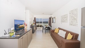 A modern living room with a TV, sofa, and dining area. - Summer Breeze Penthouse with large Terrace and Hot Tub by Getaways Malta (Mellieha)