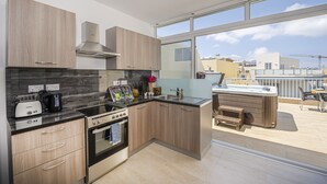 A modern kitchen with wooden cabinets, a built-in stove, and a large window overlooking a balcony. - Summer Breeze Penthouse with large Terrace and Hot Tub by Getaways Malta (Mellieha)