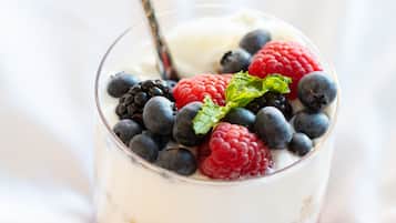 Postre en capes en un got de vidre transparent, amb una cullera, coronat amb fruita del bosque i fulles de menta.