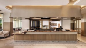 A modern bar area with a central counter, seating area, and a view of the kitchen in the background. - The Celeste Hotel, Orlando, a Tribute Portfolio Hotel (Orlando)