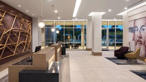 A modern lobby with a reception desk, seating area, and large windows offering views of the outdoors.