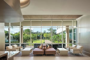 A modern lobby with large windows, a seating area with sofas and chairs, and a view of a lush garden.