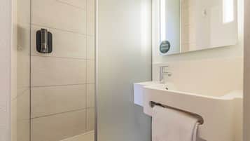 Een moderne badkamer met een glazen douchecabine, een wit wastafeltje en een handdoekhouder.