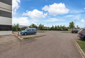 A parking lot with a blue car and a building with a modern design. - B&B HOTEL Colmar Expo (Colmar)