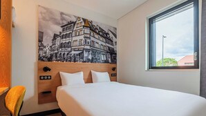Habitación de hotel con cama, cabecera con controles, ventana y una obra de arte colgada en la pared.