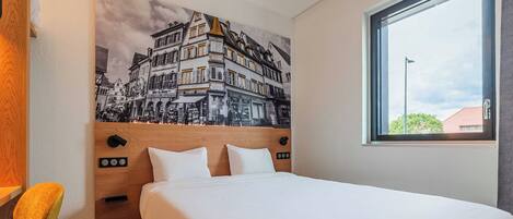 Une chambre d’hôtel comprenant un lit, une tête de lit dotée de commandes, une fenêtre et une œuvre d’art fixée au mur.