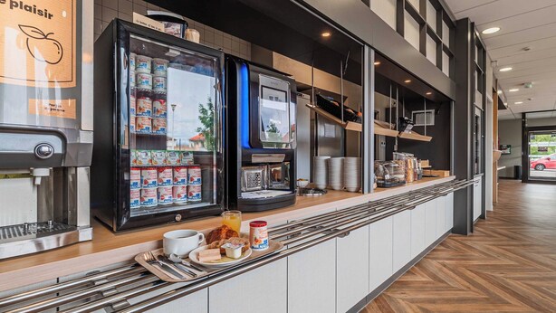 Una barra de desayuno moderna con una máquina de café, bebidas refrigeradas y una pantalla digital.
