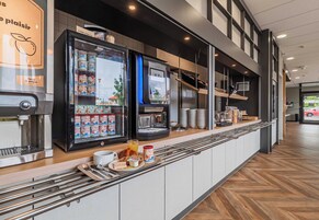 Una barra de desayuno moderna con una máquina de café, bebidas refrigeradas y una pantalla digital.
