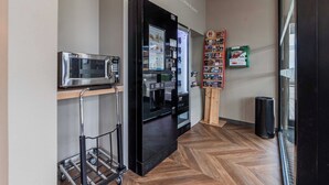 Una cocina equipada con microondas, refrigerador y máquina expendedora de bebidas.