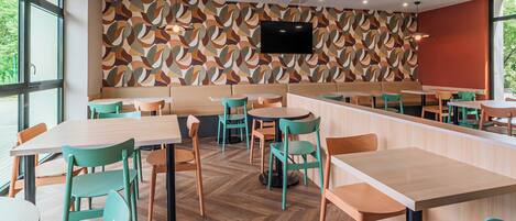 Ce restaurant est doté d’un sol en parquet à motifs chevrons, de tables vertes et en bois, ainsi que de chaises. Un téléviseur à écran plat est fixé au mur.
