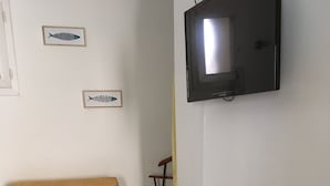 Una habitación con un sillón blanco, una mesita pequeña con un cojín con forma de pez, un control remoto y un farolillo amarillo.