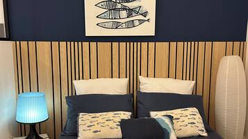 A bedroom with a bed, pillows, a wall-mounted fish painting, a bedside lamp, and a wooden headboard.