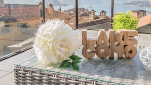 A balcony with a view of a lake and mountains, a white flower, and wooden letters spelling "LAKE COMO". - La Terrazza di Marta (Varenna)