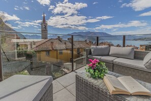 Une terrasse avec des meubles en osier, une table en verre et un livre.