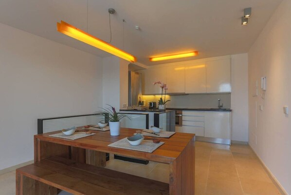 A modern kitchen with white cabinets, a wooden dining table with placemats, and pendant lighting.