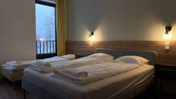 A hotel room with two beds, a wooden headboard, bedside lamps, a window with curtains, and a wooden floor.