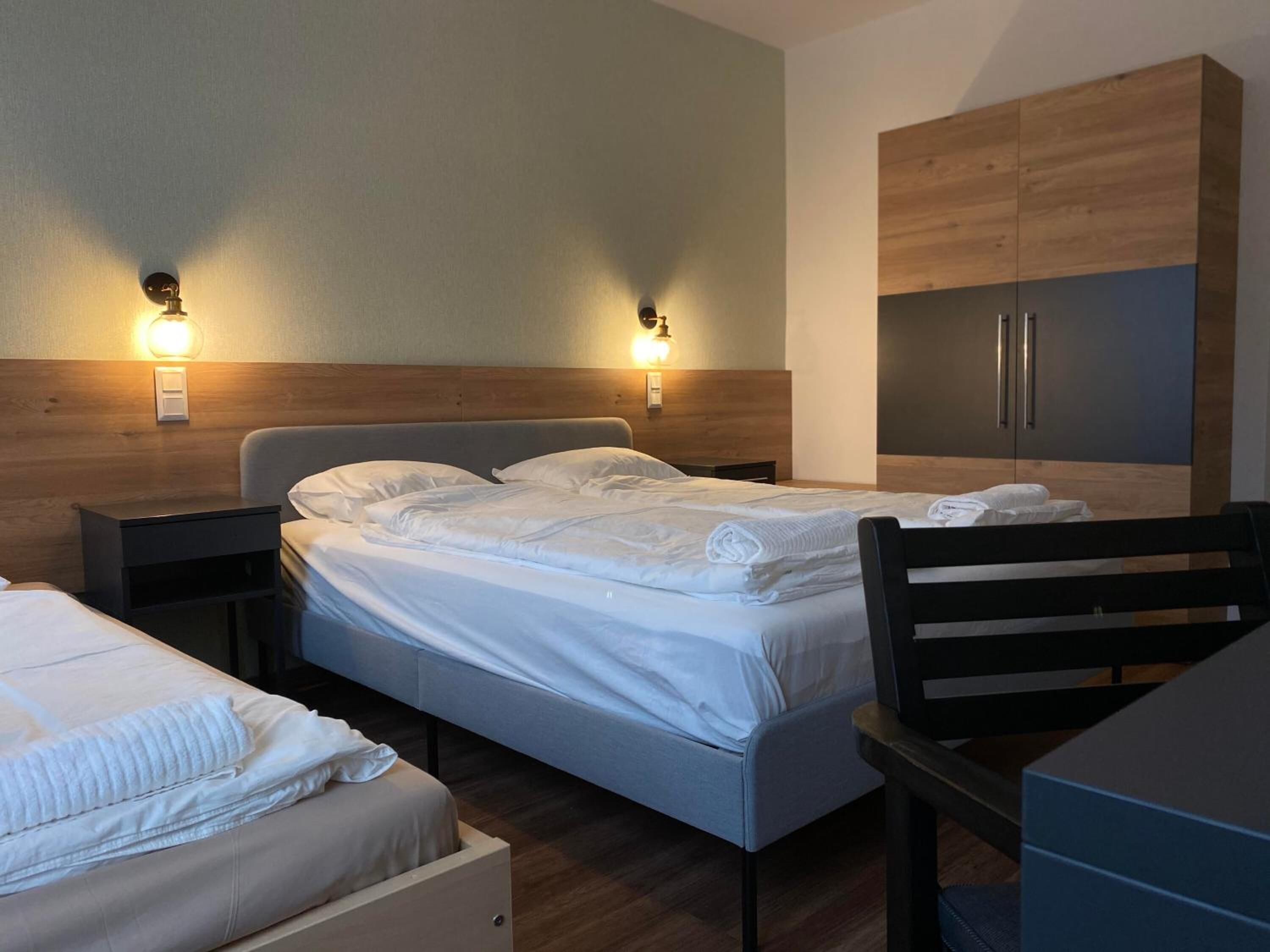 A hotel room with a bed, bedside tables, a desk, and a wardrobe.