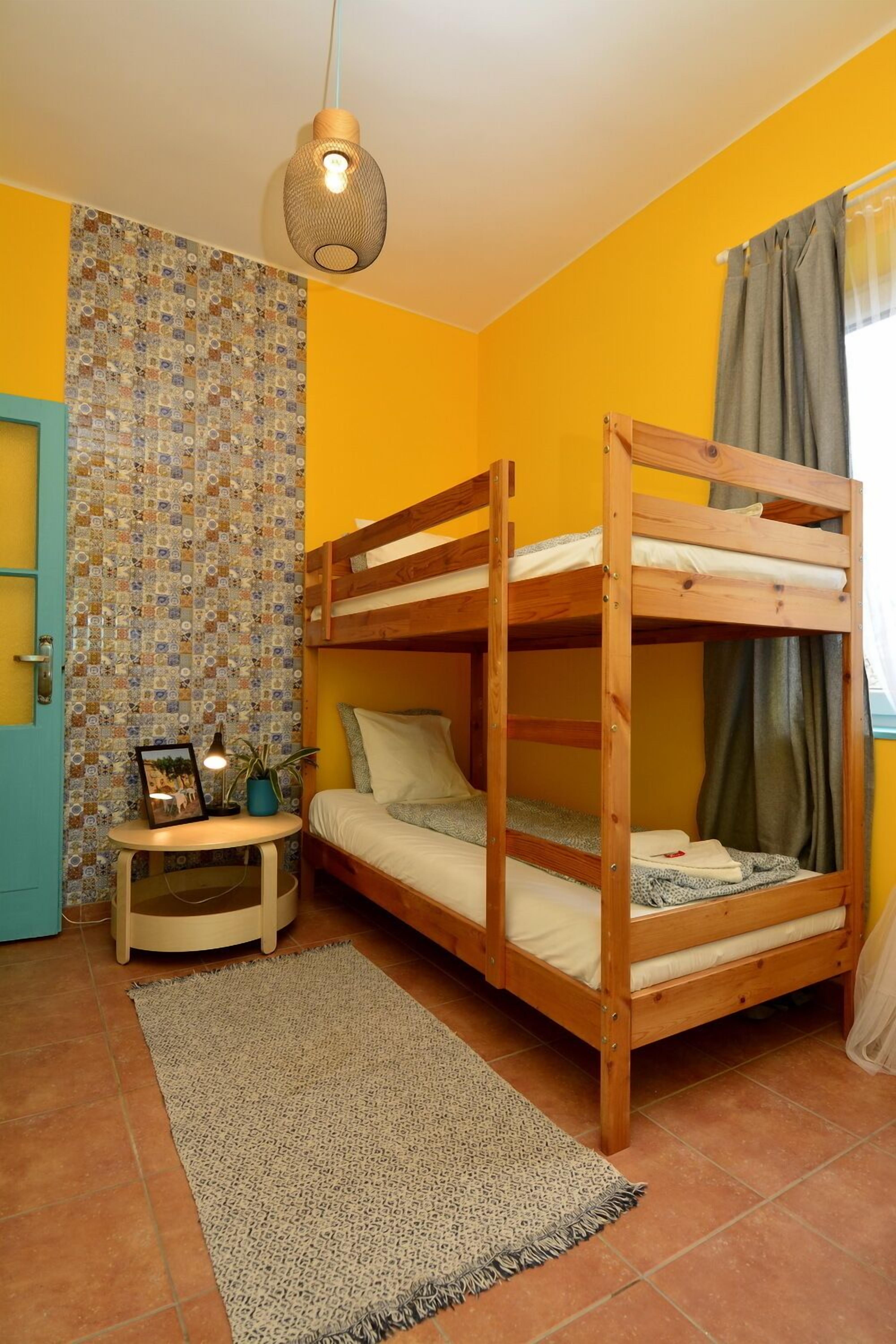 Una habitación con literas, una mesita con lámpara, un tapete estampado y una pared con diseño de mosaico.