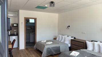 A hotel room with two beds, a desk, a small kitchenette, and a bathroom.
