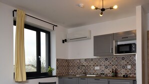A modern kitchen with grey cabinets, a wooden dining table, and a window with yellow curtains. - Ludwig Hotel (Martonvásár)
