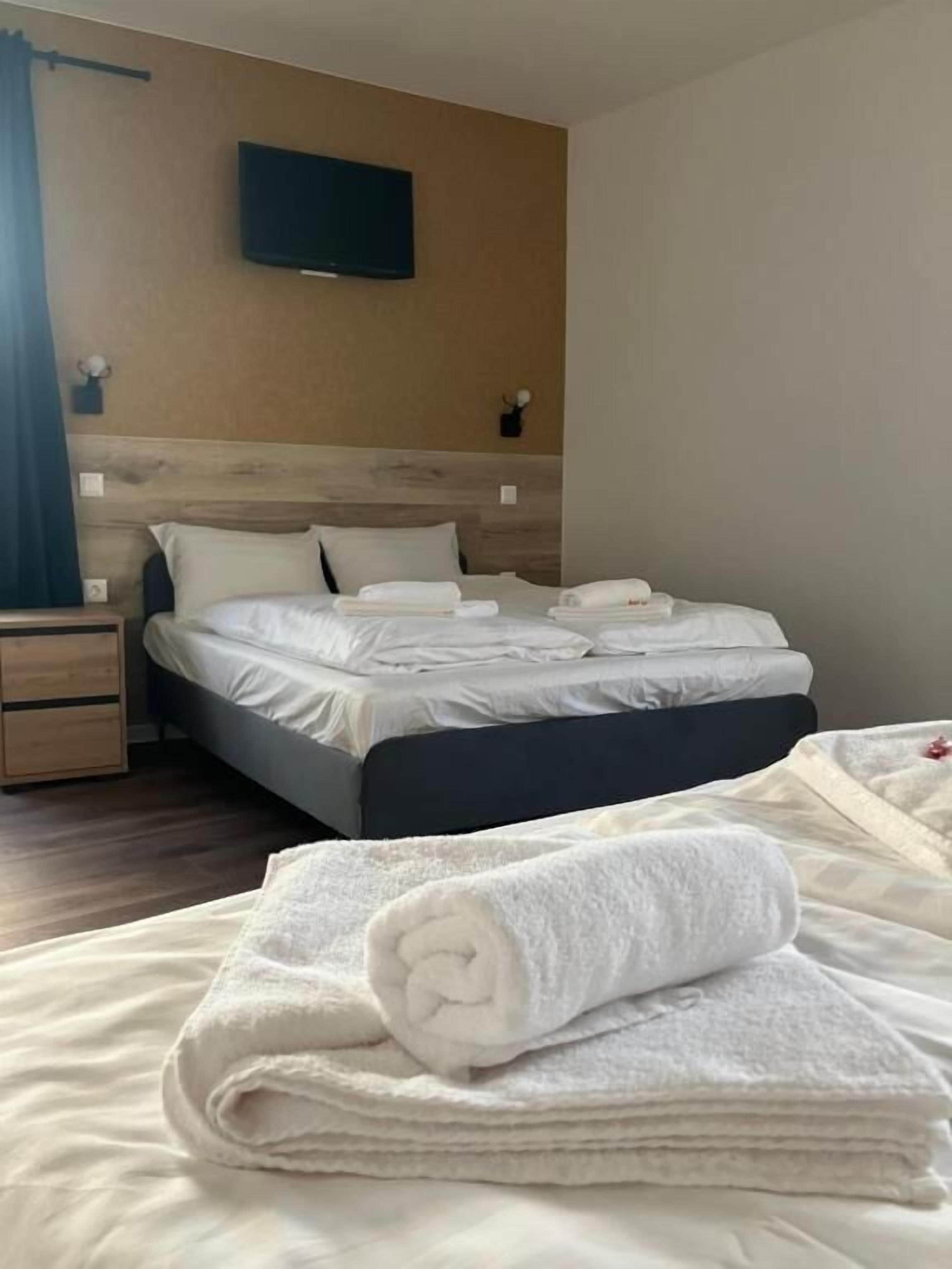 A hotel room with a bed, a nightstand, a TV mounted on the wall, and a window with curtains.