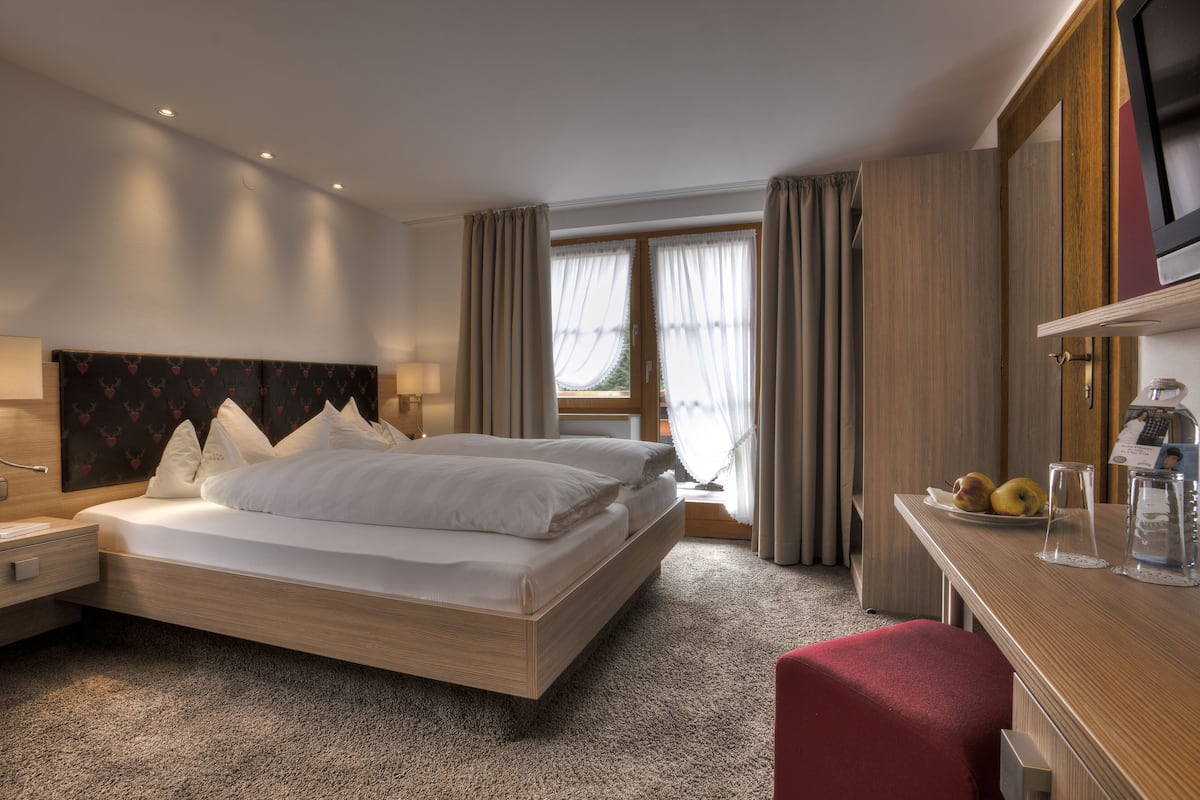 A hotel room with a large bed, a desk with a computer, a TV, and a window with curtains.