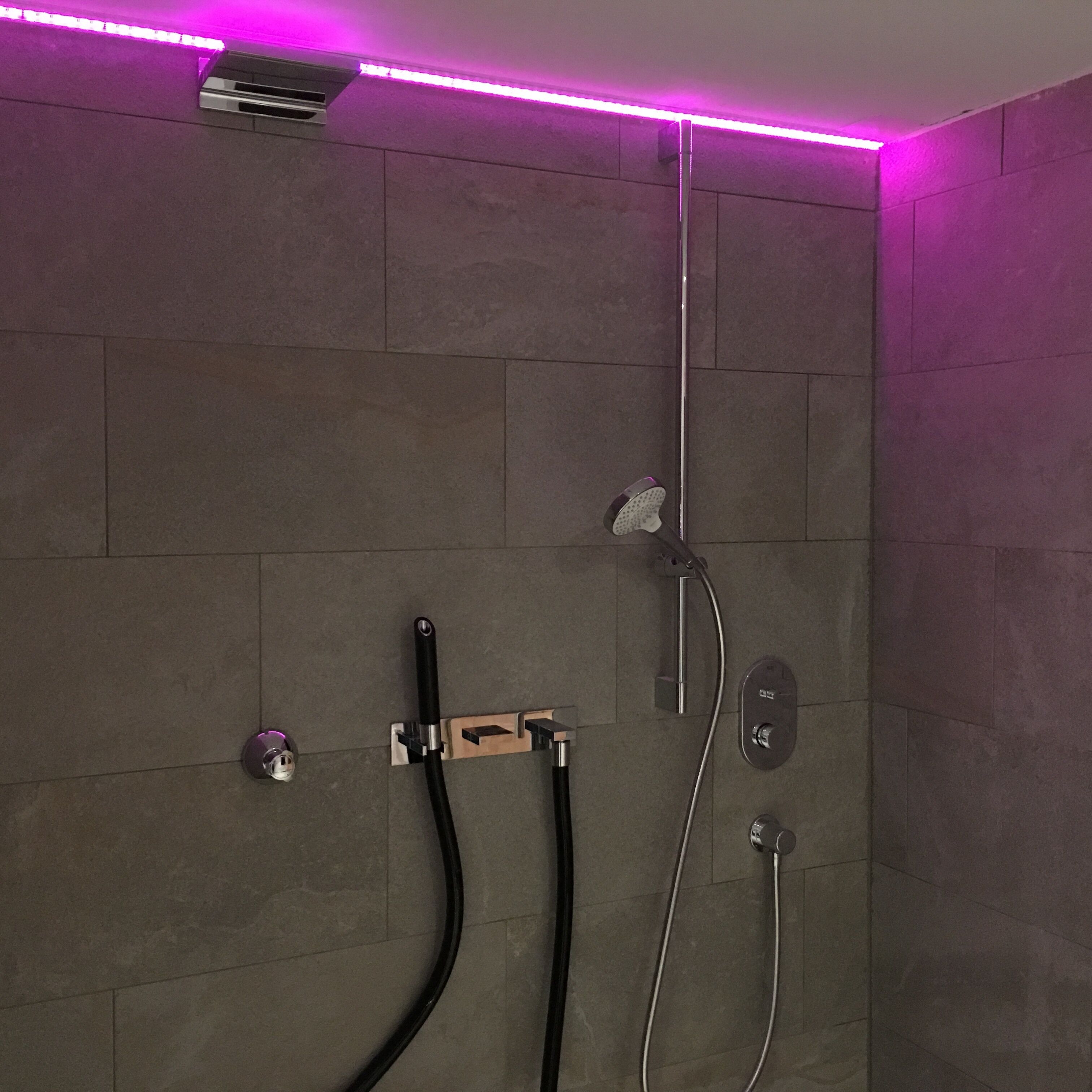 A modern shower with a handheld showerhead, a wall-mounted faucet, and a control panel.