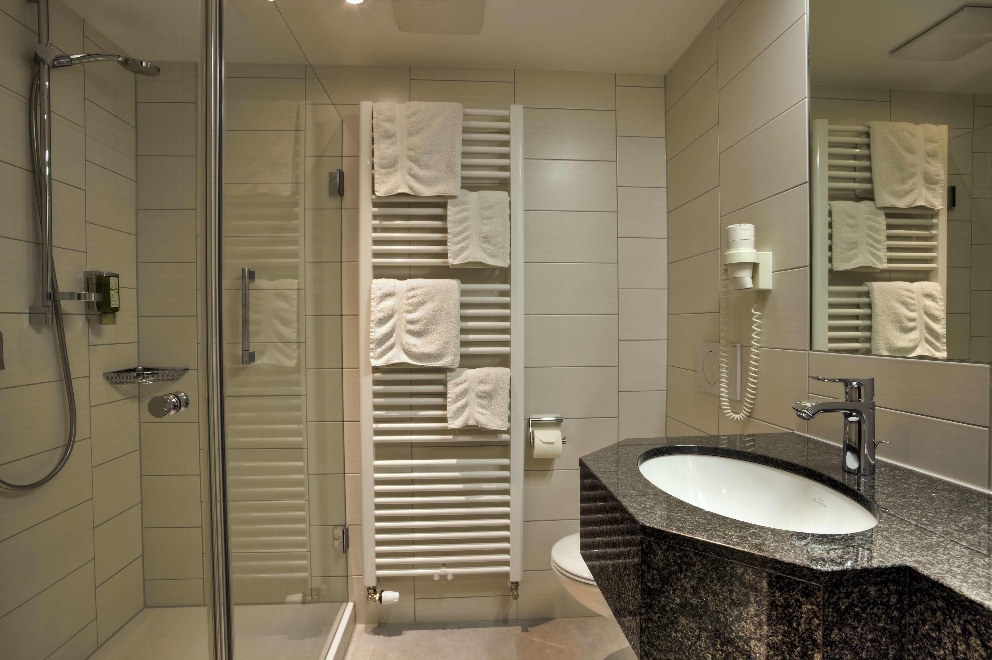 A modern bathroom with a glass shower enclosure, a granite sink, and a towel rack with multiple towels.