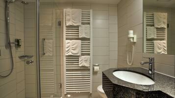 A modern bathroom with a glass shower enclosure, a granite sink, and a towel rack with multiple towels.