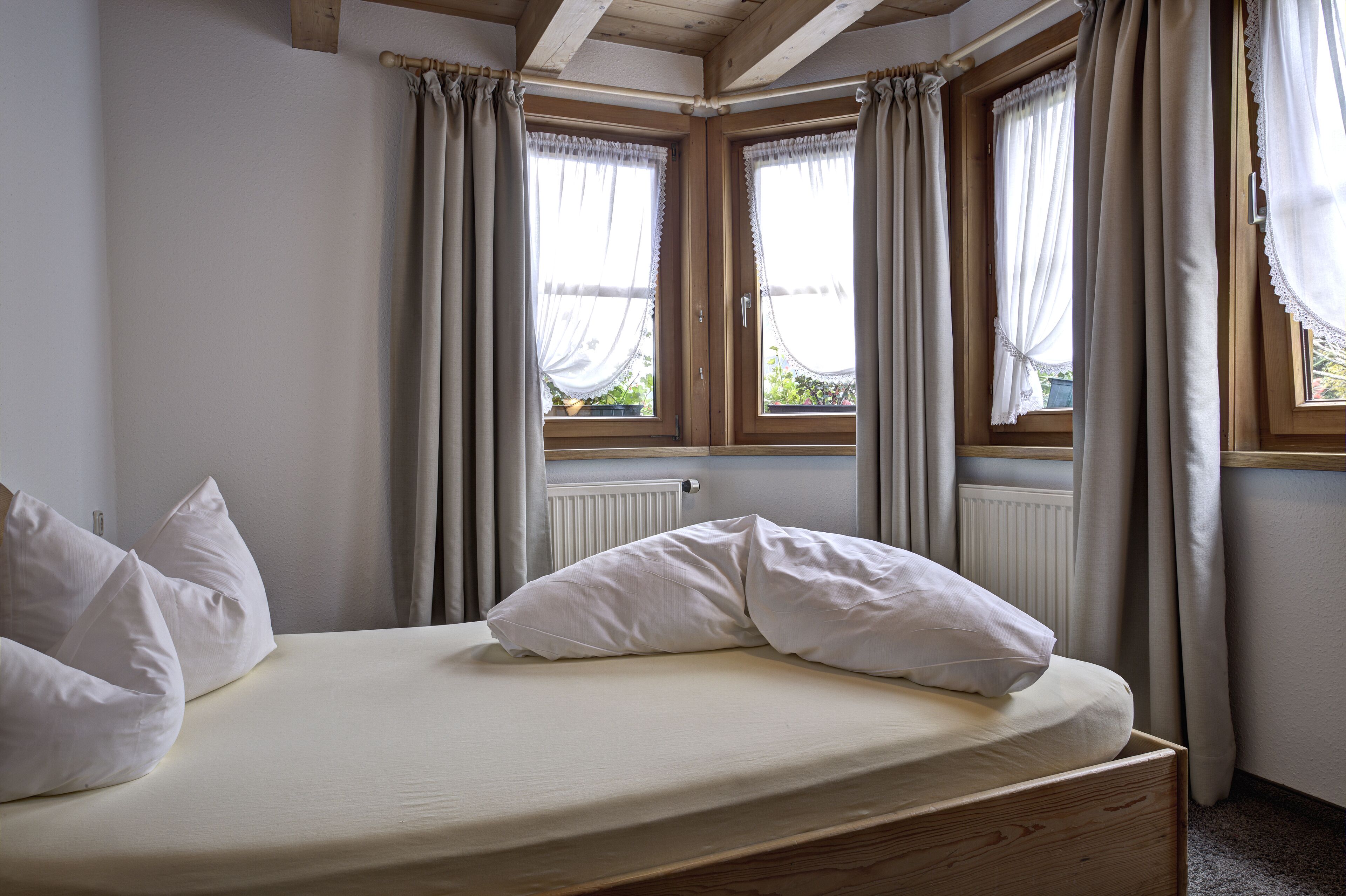 A single bed with white bedding in a room with wooden beams and a window with curtains.