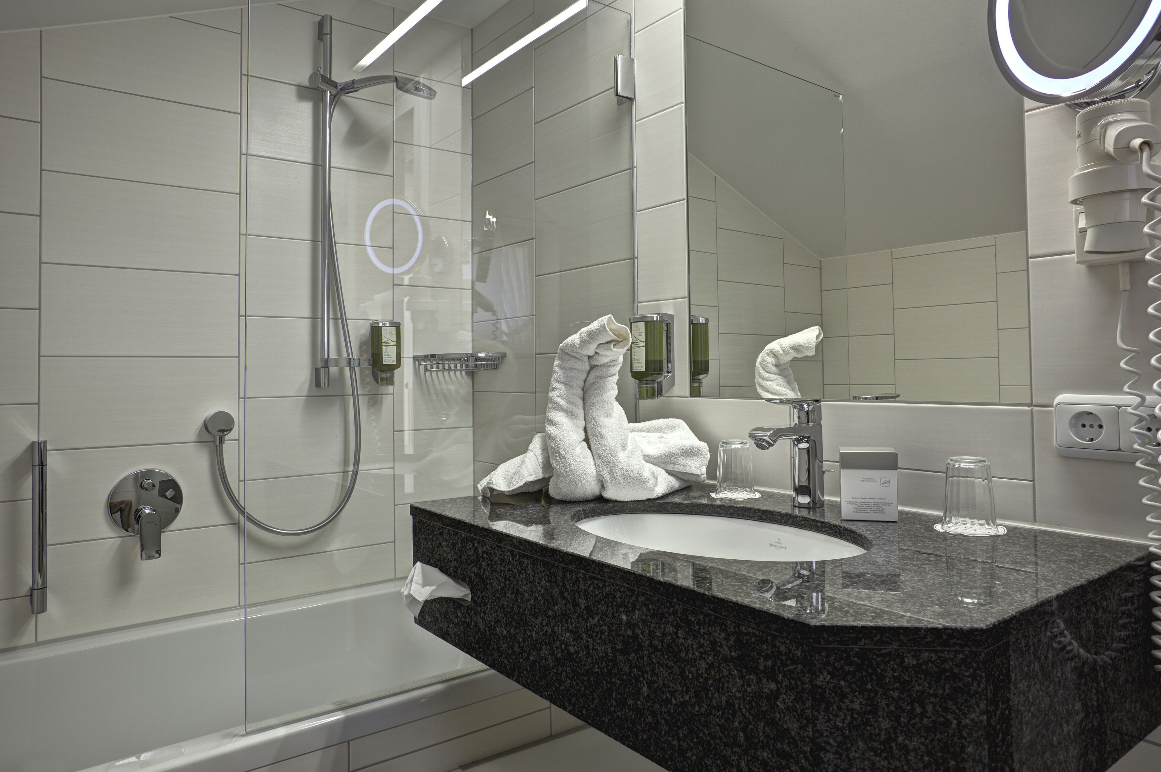A modern bathroom with a granite countertop sink, a handheld showerhead, and a large mirror with a ring light.