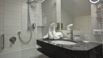 A modern bathroom with a granite countertop sink, a handheld showerhead, and a large mirror with a ring light.