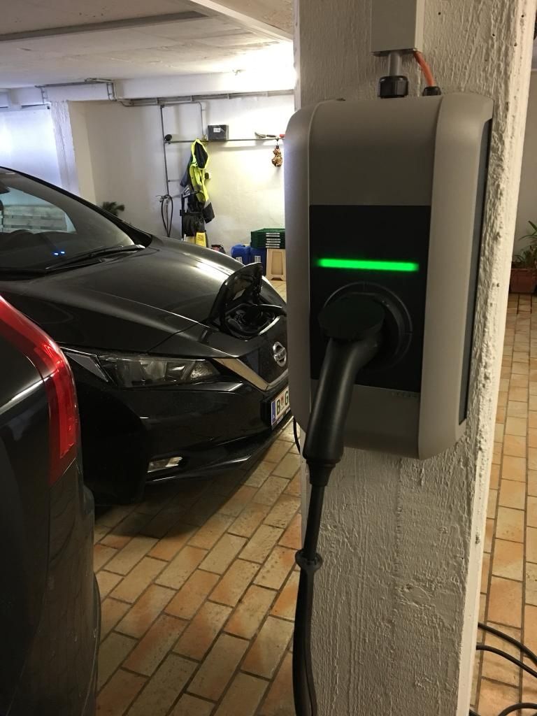 A car charging station in a garage with a black car connected to it.