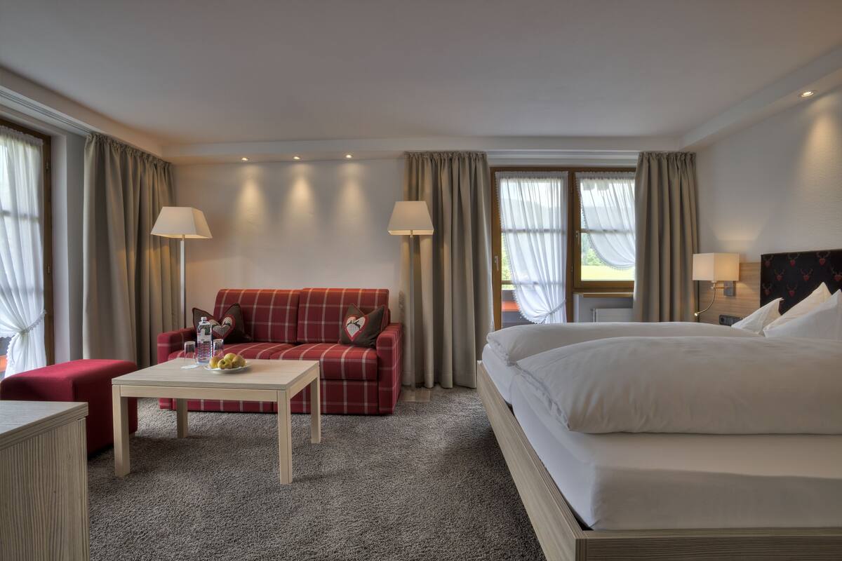 A hotel room with a bed, a red sofa, a white table, and two lamps.