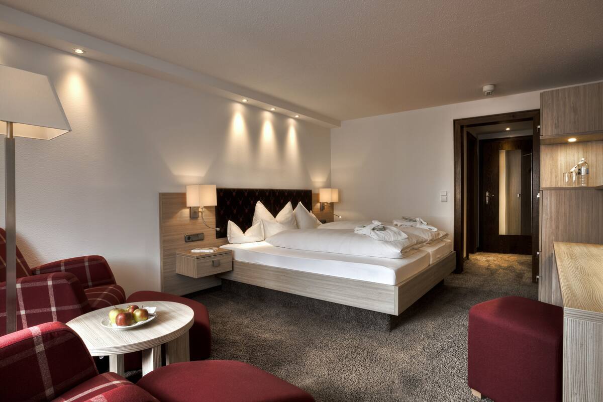 A hotel room with a bed, a nightstand, a lamp, a chair, and a small table with apples.