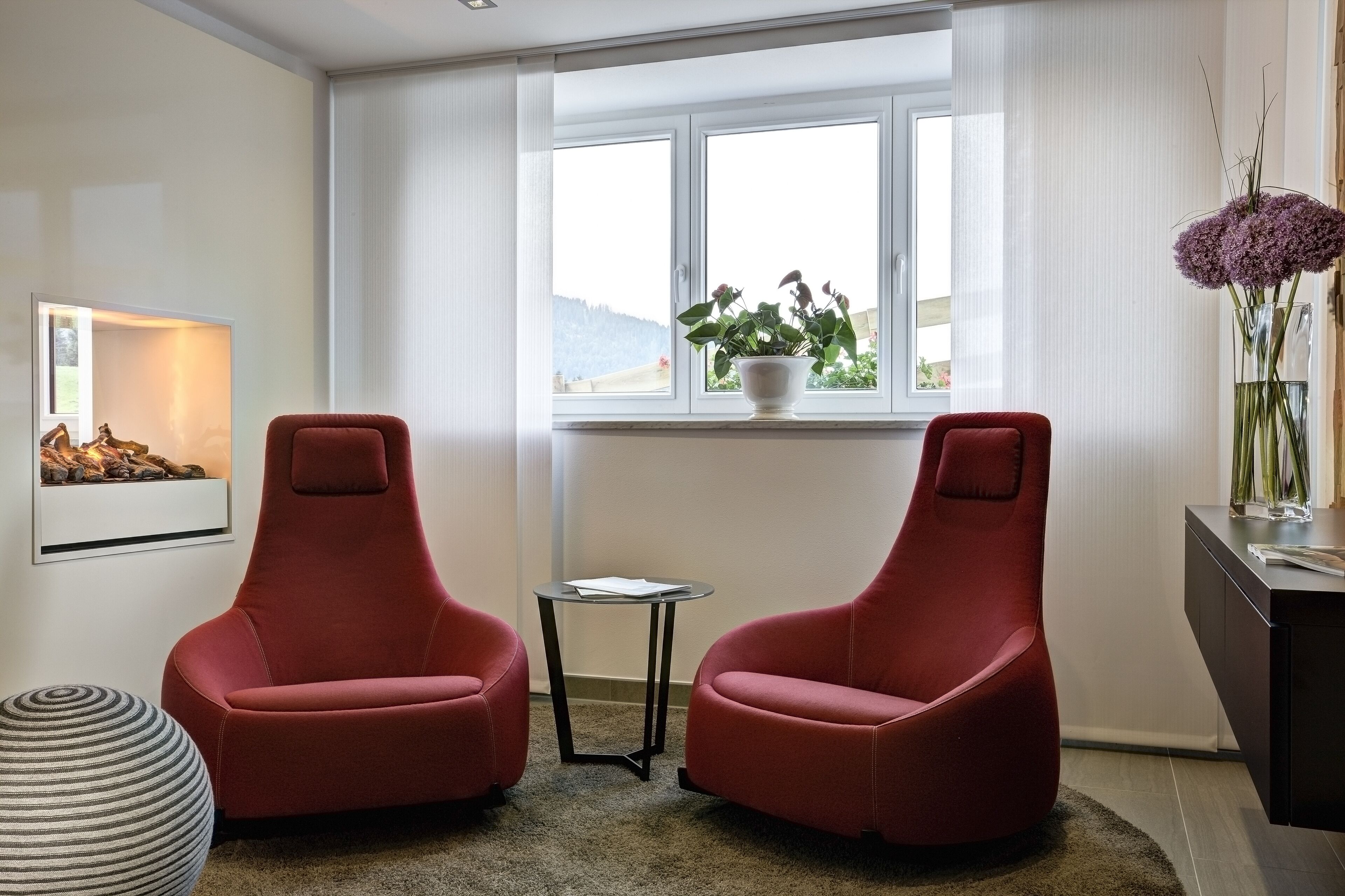 Una habitación moderna con dos sillas rojas, una mesita, una planta en maceta y una chimenea.