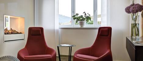 Una habitación moderna con dos sillas rojas, una mesita, una planta en maceta y una chimenea.