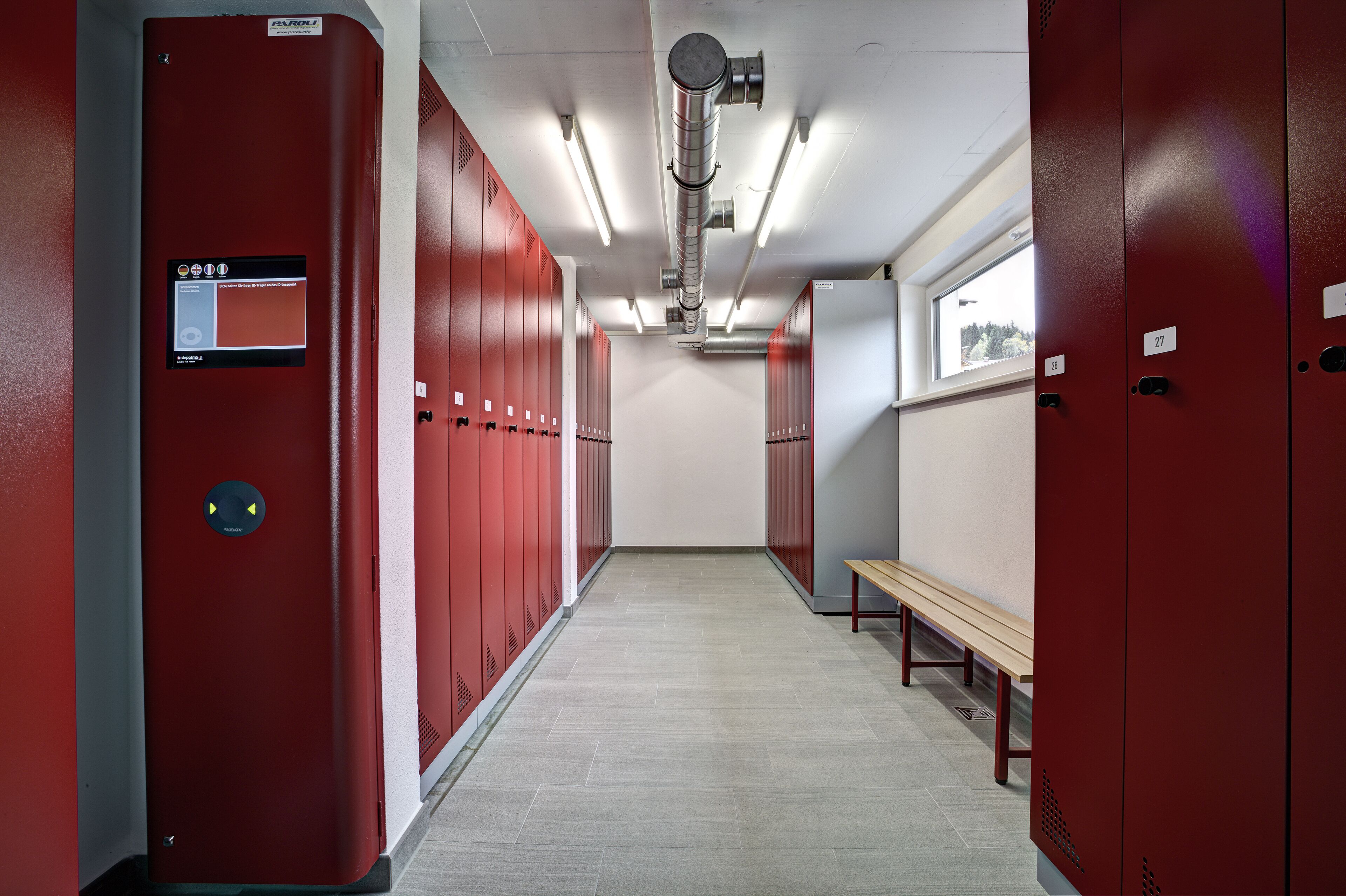 Un vestiaire avec des casiers rouges, un banc et un système de ventilation.