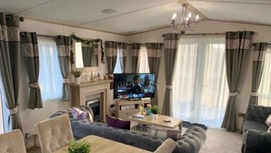 A living room with a TV, sofa, dining table, and curtains. - Sherwood Lodge - South Lakeland Leisure Village (Carnforth)