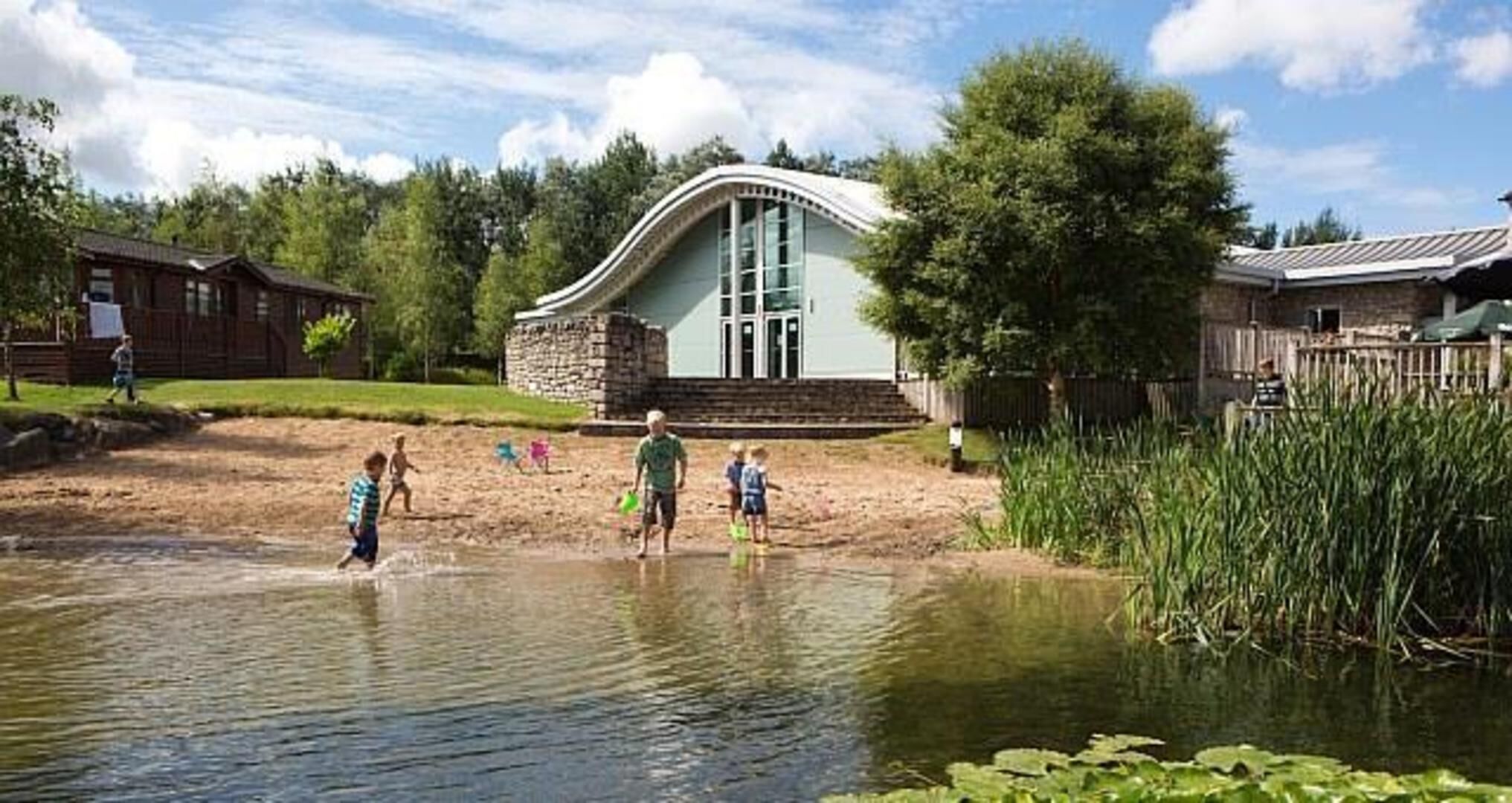 A building with a curved roof and large windows, surrounded by a grassy area and a body of water.