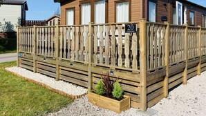 A wooden mobile home with a fenced porch, a small garden bed, and a sign indicating the number 20 Sherwood. - Sherwood Lodge - South Lakeland Leisure Village (Carnforth)