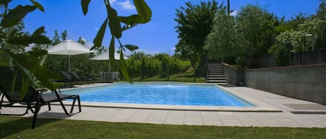 Ein rechteckiger Swimmingpool mit einer gefliesten Liegefläche, umgeben von einem Rasen und Bäumen.