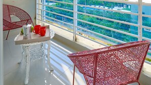 Un balcon avec des balustrades en métal blanc, une table avec des tasses rouges et une chaise.